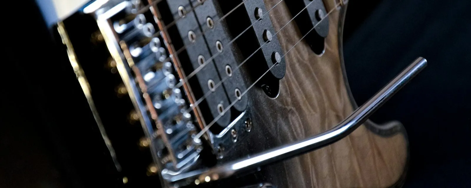 The bridge, saddles and tremolo arm of an electric guitar, lit from one side against a dark ground